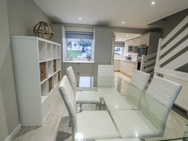 A dining room with a glass table and white chairs at White Sails Y Felinheli