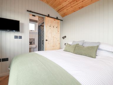A bedroom with a bed with green and gray pillows a mounted television and a wooden sliding door leading to a bathroom at Northcott Hut in Stibb near Bude
