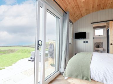 A bedroom with a bed a wall mounted tv and a sliding glass door leading outside at Northcott Hut Stibb near Bude