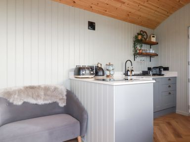 A small kitchen area with a gray sofa and fur throw at Northcott Hut Stibb near Bude