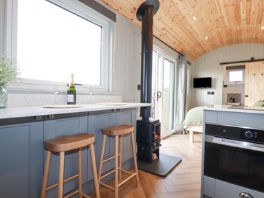 A kitchen area with wooden stools a stove and a bed visible at Northcott Hut Stibb near Bude
