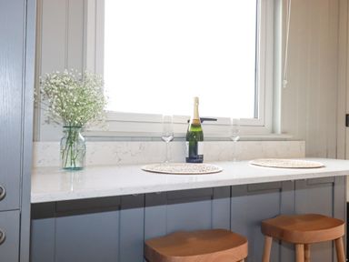 A kitchen counter with a vase of flowers a bottle and two glasses at Northcott Hut in Stibb near Bude