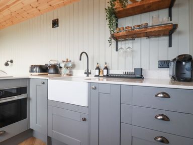 A kitchen with gray cabinets a white farmhouse sink a black faucet a toaster kettle and coffee machine on the counter at Northcott Hut in Stibb near Bude