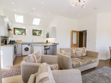 An open plan living room and kitchen with beige sofas washing machine and dining table at Little Barn in Grange-Over-Sands near Cartmel