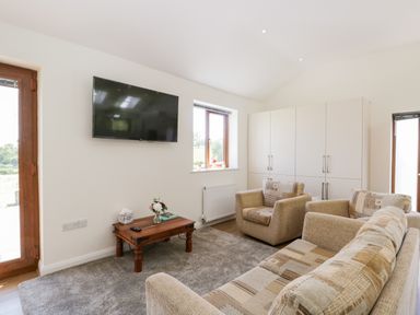 A living room with a sofa, armchairs, coffee table, wall-mounted TV, and cupboards at Little Barn in Grange-Over-Sands near Cartmel