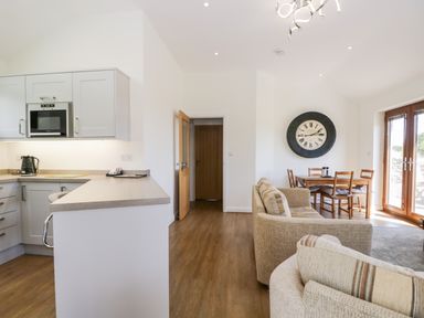 An open plan kitchen and living area with a sofa dining table and large wall clock at Little Barn in Grange-Over-Sands near Cartmel