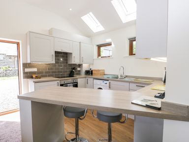 A kitchen with white cabinets a wooden countertop two bar stools and a tiled backsplash at Little Barn Grange-Over-Sands near Cartmel