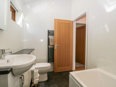 A bathroom with a sink, toilet, bathtub, and a wooden door at Little Barn in Grange-Over-Sands near Cartmel
