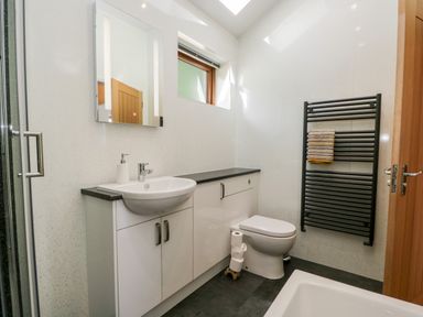 A bathroom with a sink cabinet toilet shower and a towel on a black radiator at Little Barn in Grange-Over-Sands near Cartmel