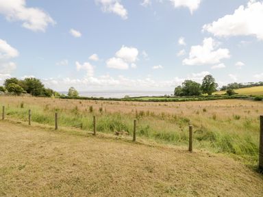 A grassy field with wooden posts and wire fencing under a blue sky with clouds at Little Barn in Grange-Over-Sands near Cartmel