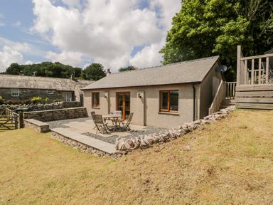 A small house with a stone patio and outdoor table and chairs at Little Barn in Grange-Over-Sands near Cartmel