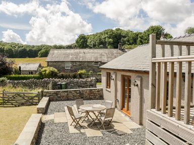 A patio with a round wooden table and four chairs next to a building with glass doors and stone walls at Little Barn in Grange-Over-Sands near Cartmel