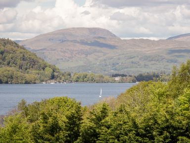 A lake with a sailboat in front of hills and trees at Little Barn in Grange-Over-Sands near Cartmel