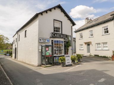 A village shop with a telephone booth and signs on a street corner in Cartmel