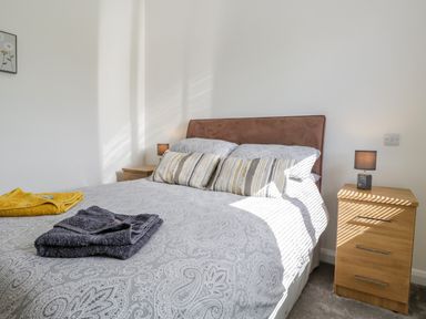 A bedroom with a bed with patterned grey bedding two bedside tables with lamps and folded towels on the bed at Little Barn in Grange-Over-Sands near Cartmel