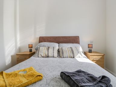 A bedroom with a double bed two striped pillows bedside tables with lamps and folded towels on the bed at Little Barn in Grange-Over-Sands near Cartmel