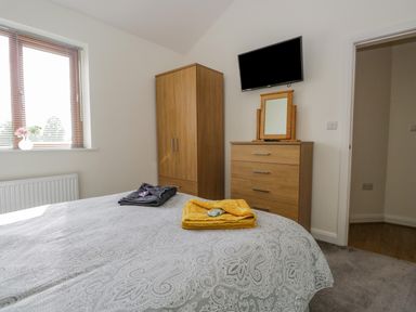 A bedroom with a bed with folded towels a wooden wardrobe and chest of drawers with a mirror and a television on the wall at Little Barn in Grange-Over-Sands near Cartmel