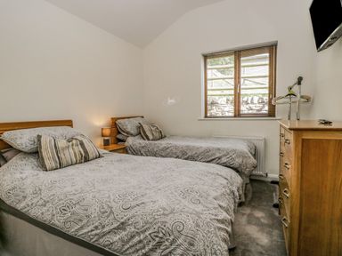 A bedroom with two single beds a wooden dresser a window with blinds and a mounted television at Little Barn in Grange-Over-Sands near Cartmel