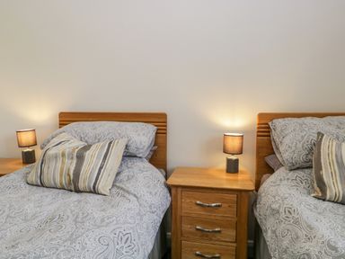 A bedroom with two single beds a wooden nightstand between them with a lit lamp on each side at Little Barn in Grange-Over-Sands near Cartmel