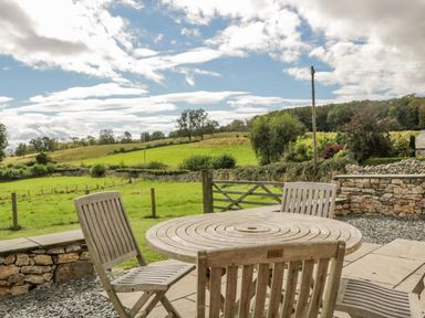 An outdoor patio with a round wooden table and four chairs overlooking a green field at Little Barn Grange-Over-Sands near Cartmel