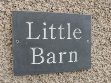 A black sign with white letters reading Little Barn mounted on a textured stone wall at Little Barn in Grange-Over-Sands near Cartmel