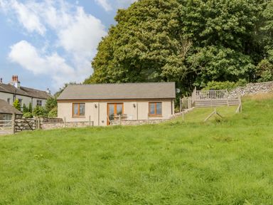 A small house with wooden windows and a grassy yard at Little Barn in Grange-Over-Sands near Cartmel