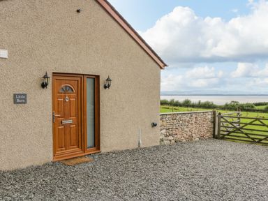 A stone exterior wall with a wooden door and a stone wall with a wooden gate beside a gravel driveway at Little Barn in Grange-Over-Sands near Cartmel