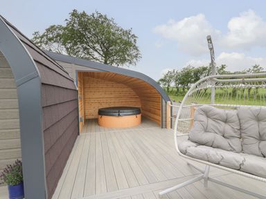An outdoor deck area with a covered hot tub and a cushioned hanging chair at Laird Lodge 1 in Lochmaben