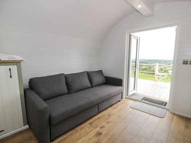 A room with a grey sofa wooden floor and an open door leading to an outdoor area at Laird Lodge 1 in Lochmaben