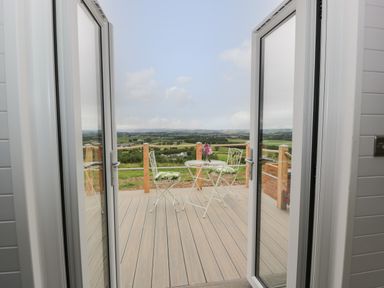A patio with a small round table and two chairs with cushions overlooking a countryside view at Laird Lodge 1 in Lochmaben