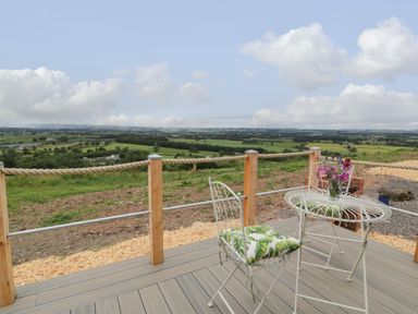An outdoor deck with a metal table and chair with cushions overlooking green fields at Laird Lodge 1 in Lochmaben