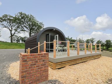 A small wooden pod with a deck featuring outdoor chairs and a swing at Laird Lodge 1 in Lochmaben