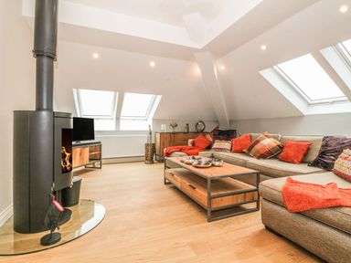 A living room with a wood stove a sectional sofa with cushions and a wooden coffee table at Sardis Chapel 1 in Malltraeth