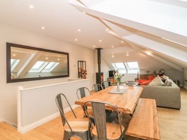 A dining area with a wooden table and metal chairs next to a living room with a sofa and skylights at Sardis Chapel 1 in Malltraeth