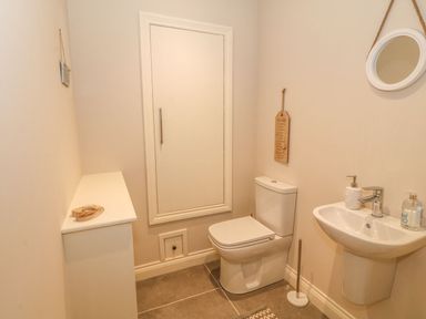 A small bathroom with a toilet a wall-mounted sink and a round mirror at Sardis Chapel 1 in Malltraeth