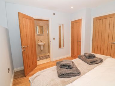 A bedroom with a bed covered in beige and white bedding and folded grey towels on top with three wooden doors and an open bathroom door at Sardis Chapel 1 in Malltraeth