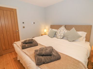 A bedroom with a bed made with white sheets and a brown throw with folded towels on it at Sardis Chapel 1 in Malltraeth