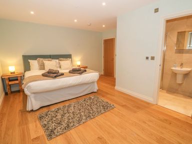 A bedroom with a double bed bedside tables lamps a rug wooden flooring and an en suite bathroom at Sardis Chapel 1 in Malltraeth