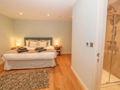 A bedroom with a bed pillows bedside tables lamps a rug and an en suite shower at Sardis Chapel 1 in Malltraeth