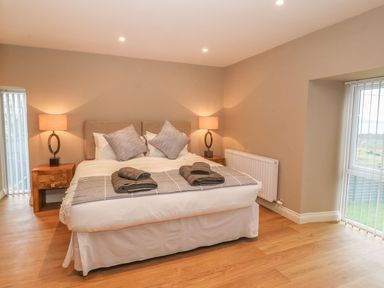 A bedroom with a double bed two bedside tables with lamps wooden floor and large windows at Sardis Chapel 1 Malltraeth
