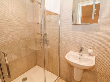 A bathroom with a glass shower enclosure a wall-mounted shower head a white sink with a faucet and soap dispenser at Sardis Chapel 1 in Malltraeth