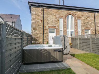 An outdoor space with a hot tub next to a stone building and fenced patio at Sardis Chapel 1 in Malltraeth