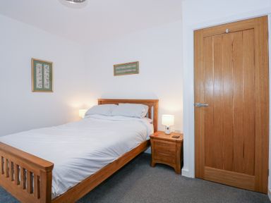 A bedroom with a double wooden bed bedside table with lamp wooden door and framed artwork on white walls at Escape To The Chapel Anglesey Bryngwran near Rhosneigr