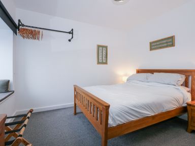 A bedroom with a wooden bed white bedding framed pictures on the wall hangers on a rail and a window seat at Escape To The Chapel Anglesey Bryngwran near Rhosneigr