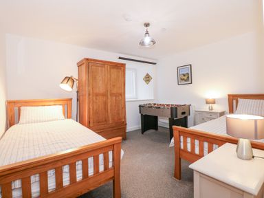 A bedroom with two single beds a wooden wardrobe a foosball table and bedside tables with lamps at Escape To The Chapel Anglesey Bryngwran near Rhosneigr