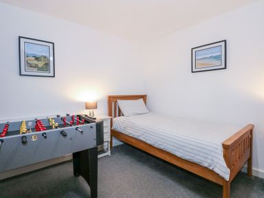 A bedroom with a single wooden bed a foosball table a bedside table with a lamp and framed pictures on the wall at Escape To The Chapel Anglesey Bryngwran near Rhosneigr