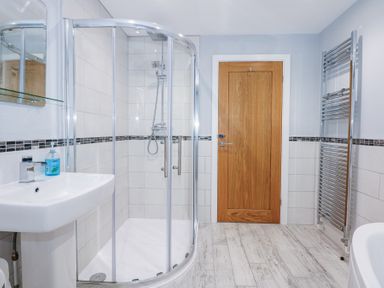A bathroom with a corner shower enclosure a white sink a wooden door and a chrome heated towel rail at Escape To The Chapel Anglesey Bryngwran near Rhosneigr
