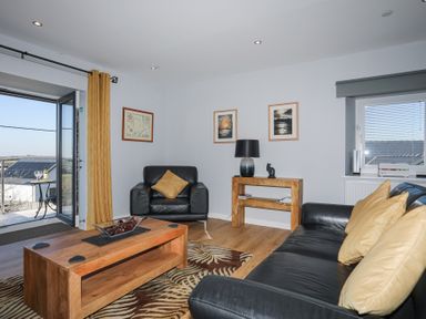 A living room with black leather sofa and armchair with yellow pillows a wooden coffee table a wooden console table with a lamp and cat figurine and open double doors to a balcony at Escape To The Chapel Anglesey Bryngwran near Rhosneigr