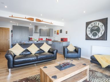 A living room with black leather sofas a wooden coffee table and a kitchen with grey cabinets at Escape To The Chapel Anglesey Bryngwran near Rhosneigr
