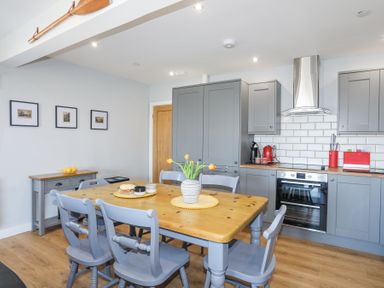 A kitchen with grey cabinets wooden dining table with six chairs and a vase of flowers at Escape To The Chapel Anglesey Bryngwran near Rhosneigr